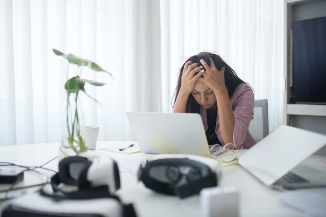 Women leans over her desk with head in hands, computer in front of her